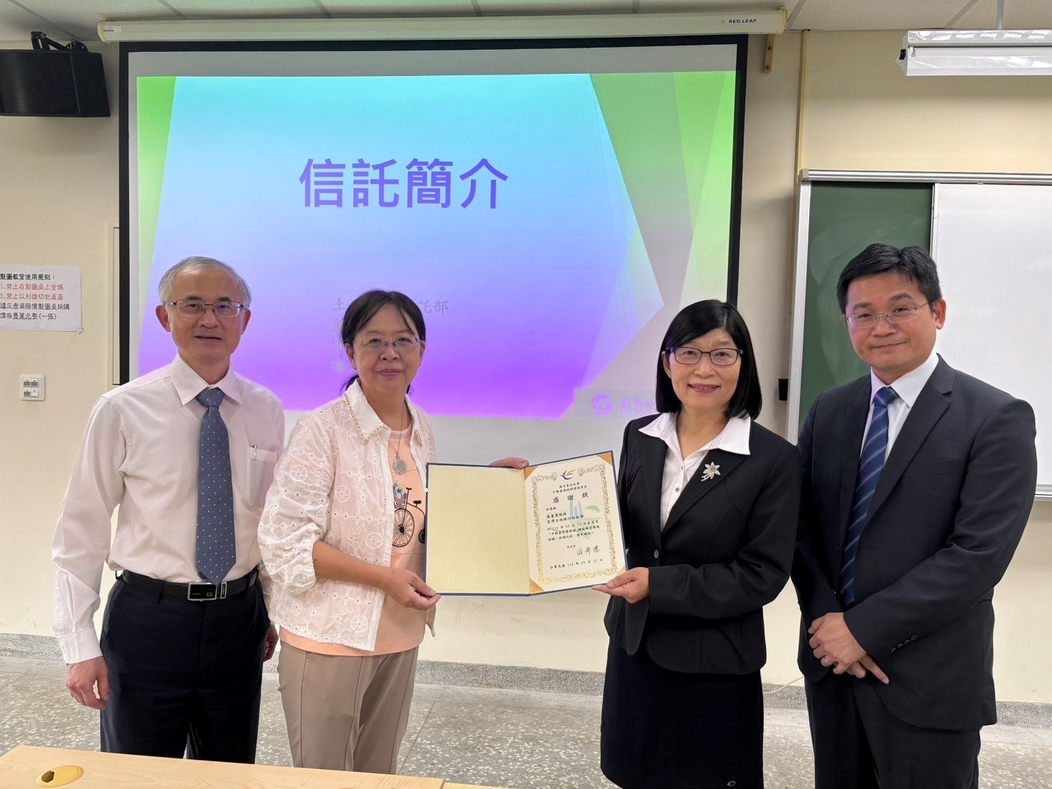 國立臺北大學不動產與城鄉環境學系林秋綿副教授（左二）致贈感謝狀予本行信託部經理蘇麗惠（右2）合影。